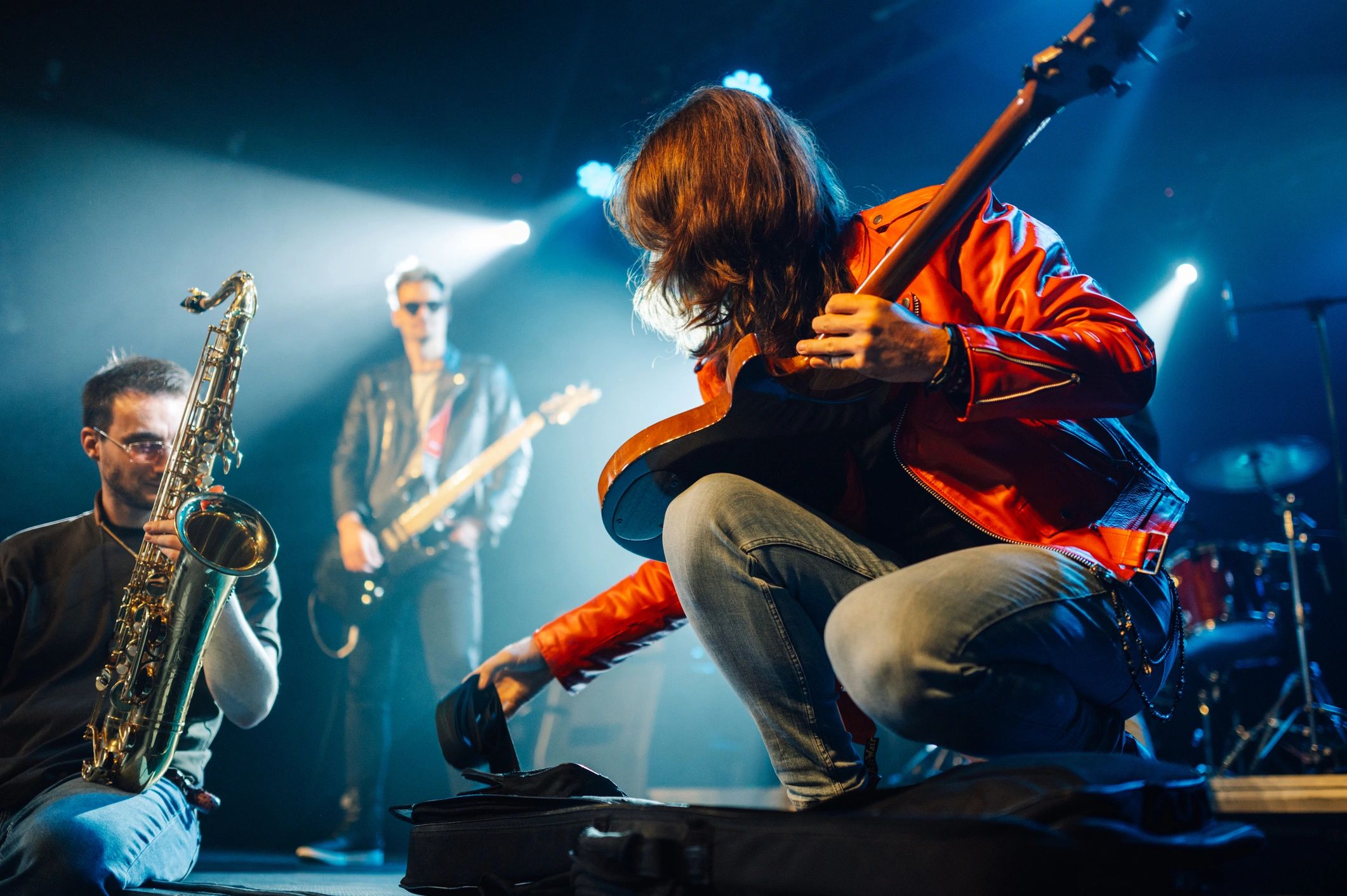 Guitarist in an orange jacket bending down to